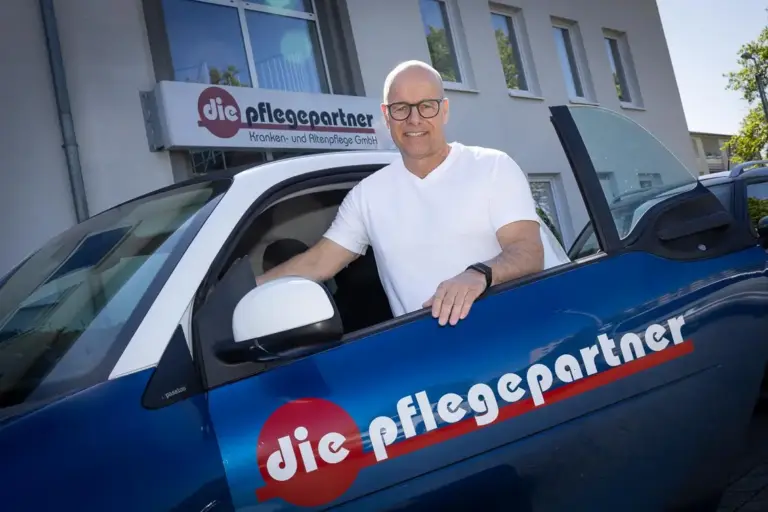 Geschäftsführer der Pflegepartner steht lächelnd an einem Dienstwagen vor dem Firmengebäude.