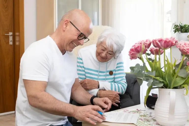 Pflegeberater bespricht mit einer Seniorin Unterlagen zum Beratungseinsatz in ihrer Wohnung.