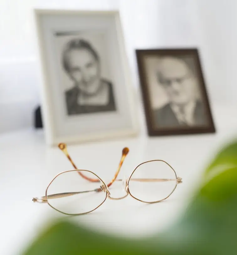 Eine Brille liegt vor zwei gerahmten Schwarz-Weiß-Fotografien auf einem Tisch.